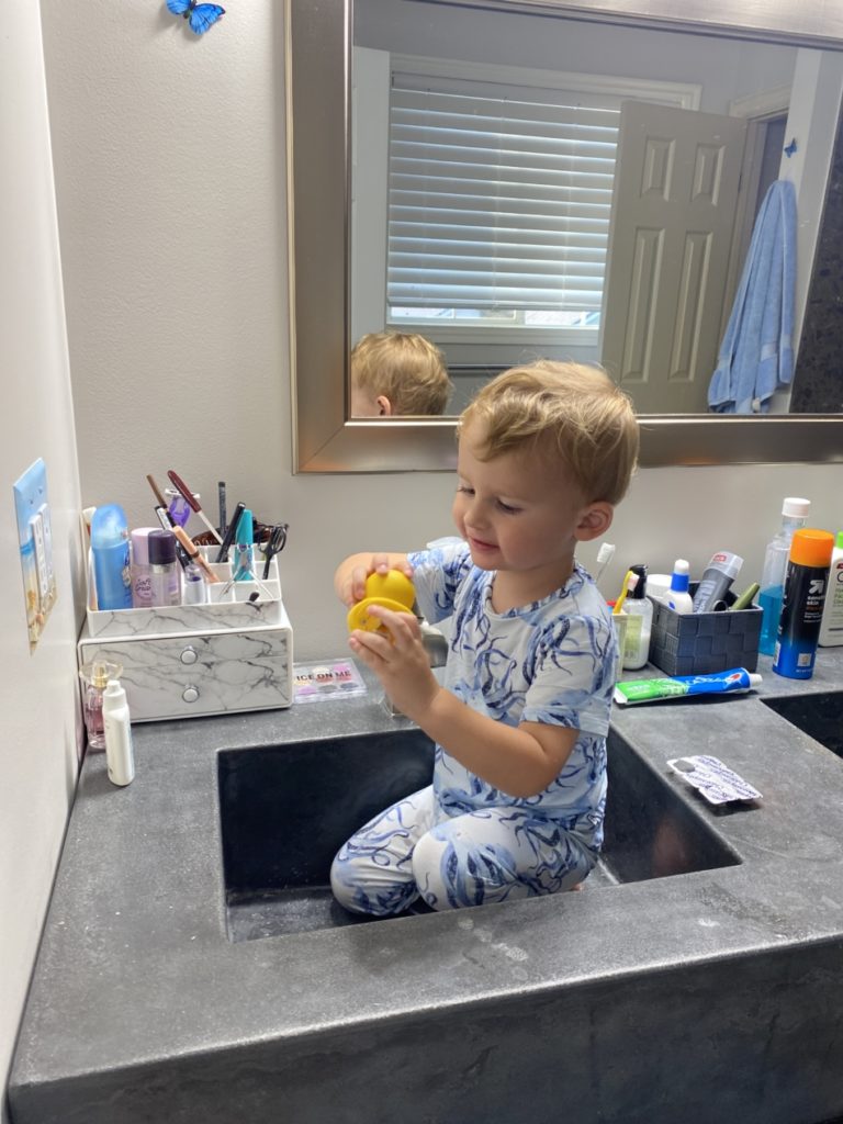A child sitting in the sink in his bamboo pajamas