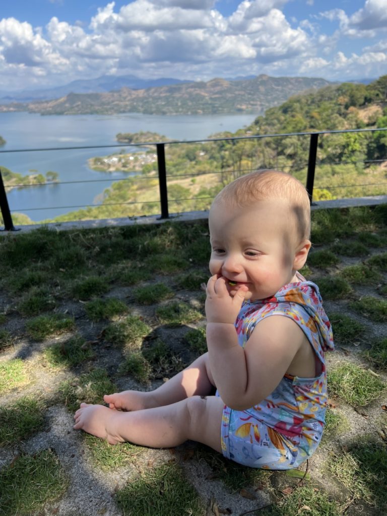 A baby sitting up in front of a lake in El Salvador