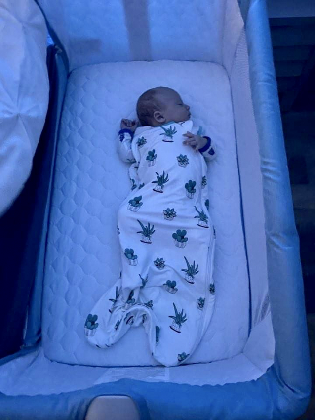 A baby sleeping in a bassinet, wearing a bamboo sleep sack from Kyte Baby
