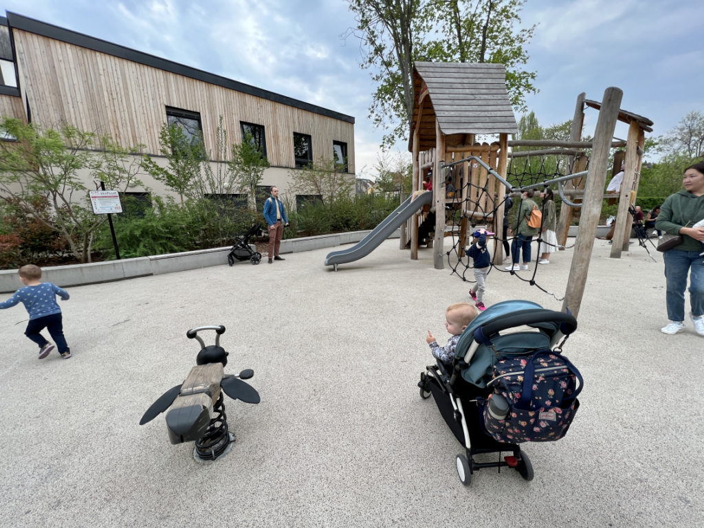 A baby sitting in a stroller at a playground in France